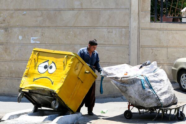 عامل نظافة يقوم بتفريغ سلة القمامة المرسوم عليها كمامة، في إطار حملة لنشر الوعي حول جائحة كورونا، في حي جنوبي بالعاصمة الإيرانية طهران في 18 يوليو 2020. - سبوتنيك عربي