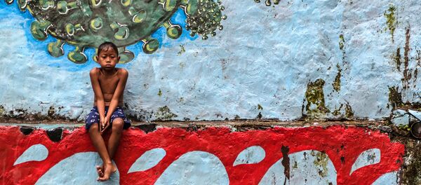 طفل يجلس أمام لوحة جدارية تمثل فيروس كورونا المسبب لمرض كوفيد -19 في بوكور، جاوة الغربية بإندونيسيا، 27 سبتمبر 2020 - سبوتنيك عربي