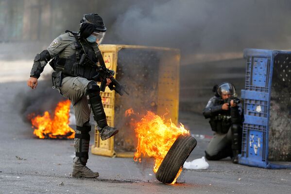 شرطي من حرس الحدود الإسرائيلي يركل عجلة مشتعلة خلال احتجاجات الفلسطينيين ضد إسرائيل في الخليل، الضفة الغربية، 23 أكتوبر 2020 - سبوتنيك عربي