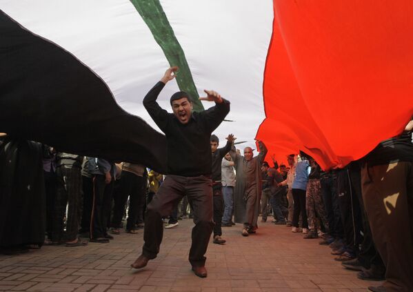 محتجون يهتفون بشعارات مناهضة للحكومة العراقية تحت علم عراقي ضخم، خلال مظاهرة في ساحة التحرير في بغداد، العراق  23 فبراير 2011 - سبوتنيك عربي