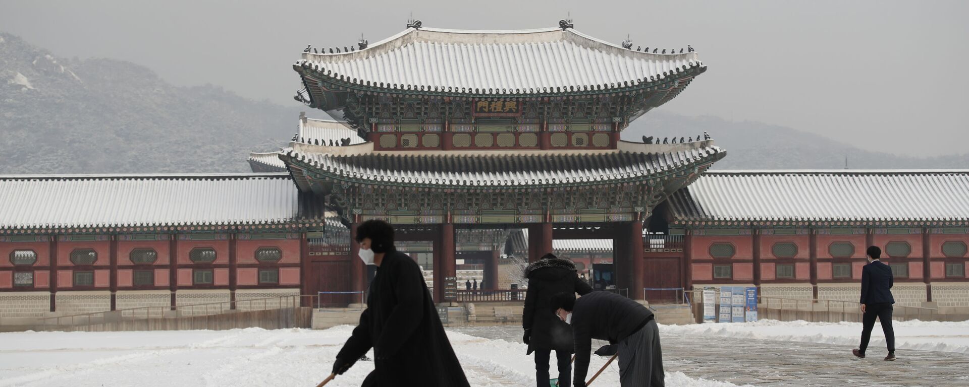 أشخاص يرتدون كمامات كإجراء احترازي ضد فيروس كورونا يقومون بإزالة الثلوج في قصر غيونغبوك، أحد المعالم المعروفة في كوريا الجنوبية، في سيئول، 13 يناير 2021. - سبوتنيك عربي, 1920, 25.09.2021