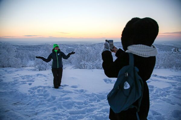 فتاة تلتقط صورة لصديقتها أثناء الفجر الأول بعد الليلة القطبية على جبل سولنيتشنايا في مورمانسك، 11 يناير 2021 - سبوتنيك عربي