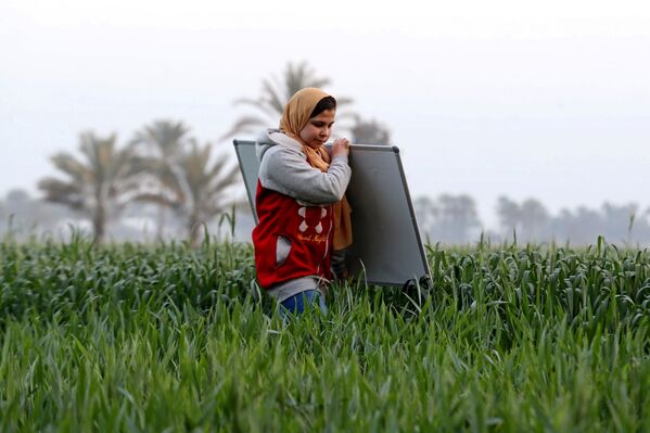 ريم الخولي، 12 عامًا، تحمل لوحا إلى موقع تعليم الأطفال في حيها حيث لاتزال المدارس مغلقة وسط جائحة فيروس كورونا (كوفيد-19)، في قرية إتميدة بمحافظة الدقهلية، مصر، 7 فبراير 2021 - سبوتنيك عربي