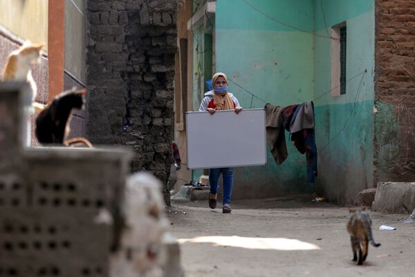 ريم الخولي، 12 عامًا، تحمل لوحا إلى موقع تعليم الأطفال في حيها حيث لاتزال المدارس مغلقة وسط جائحة فيروس كورونا (كوفيد-19)، في قرية إتميدة بمحافظة الدقهلية، مصر، 7 فبراير 2021 - سبوتنيك عربي