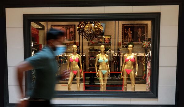 رجل يرتدي كمامة يركض أمام متجر فاخر يعرض زي السباحة بيكيني، في نخلة الجميرة في دبي، الإمارات 24 فبراير 2021 - سبوتنيك عربي