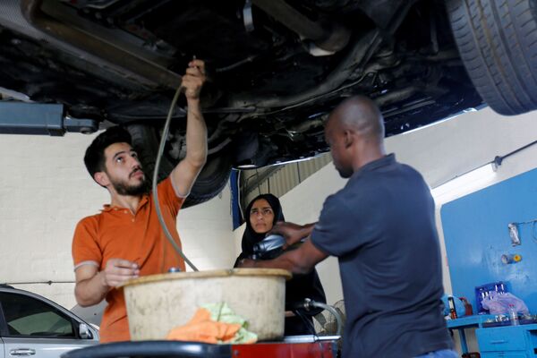 الإماراتية هدى المطروشي، 36 عاماً، مع فريق عملها أثناء تصليح سيارة في كراجها في الشارقة، الإمارات العربية المتحدة، 21 أبريل 2021 - سبوتنيك عربي