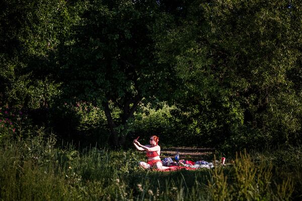 امرأة تلتقط صورة سيلفي خلال حمام شمسي بالقرب من بيحرات بوريسوفسكيه في موسكو، حيث وصلت درجة الحرارة في ذلك اليوم إلى 30 درجة مئوية، روسيا 20 يونيو 2021 - سبوتنيك عربي