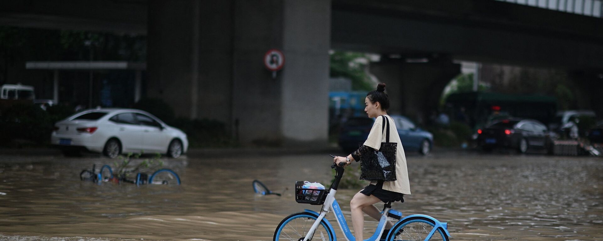 فتاة تعبر الشارع بواسطة دراجتها في أحد شوارع مدينة تشنغتشو التي غمرتها مياه الفيضانات، وسط محافظة هينان، الصين 22 يوليو 2021 - سبوتنيك عربي, 1920, 22.08.2021