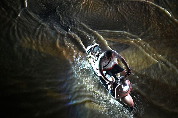 رجل يعبر الشارع بواسطة دراجته النارية في أحد شوارع مدينة تشنغتشو التي غمرتها مياه الفيضانات، وسط محافظة هينان، الصين 21 يوليو 2021 - سبوتنيك عربي