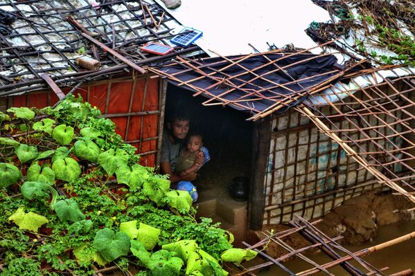لاجئ من الروهينغا يجلس مع طفله داخل مأواه الذي غمرته المياه بعد هطول أمطار غزيرة في مخيم الروهينغا للاجئين في كوتوبالونغ، بنغلاديش، 28 يوليو  2021 - سبوتنيك عربي