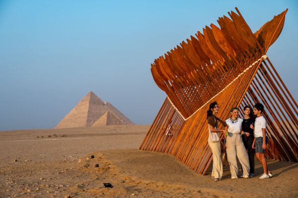 سياح يقفون بالقرب من تركيب فني بعنوان بطرخ للفنان المصري معتز نصر، في معرض الأبد هو الآن على خلفية الأهرامات في الجيزة، مصر 23 أكتوبر 2021. - سبوتنيك عربي
