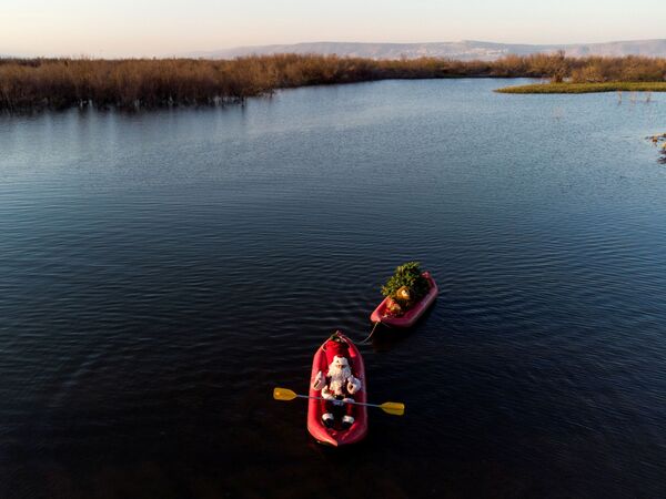 عيسى قسيسية، يرتدي زي بابا نويل، يجلس في طوف يسحب الهدايا وشجرة عيد الميلاد في حدث نظمته وزارة السياحة الإسرائيلية، حيث تستعد البلاد لموسم الأعياد، في بحيرة طبريا، شمال إسرائيل، 10 نوفمبر 2021 . - سبوتنيك عربي