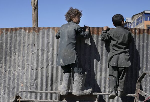 أولاد أفغان ينظرون فوق حاجز حديدي عند الأشخاص الذين يتلقون الإمدادات الغذائية أثناء توزيع المساعدات الإنسانية للعائلات المحتاجة في كابول، أفغانستان، 16 فبراير 2022. - سبوتنيك عربي