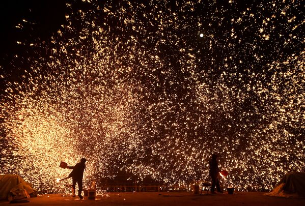 يقوم الحدادون برمي المعدن المنصهر لخلق وابل من الشرر، عشية عيد الفوانيس، الذي يصادف نهاية احتفالات السنة القمرية الجديدة، في حديقة في بكين، الصين 15 فبراير 2022. - سبوتنيك عربي