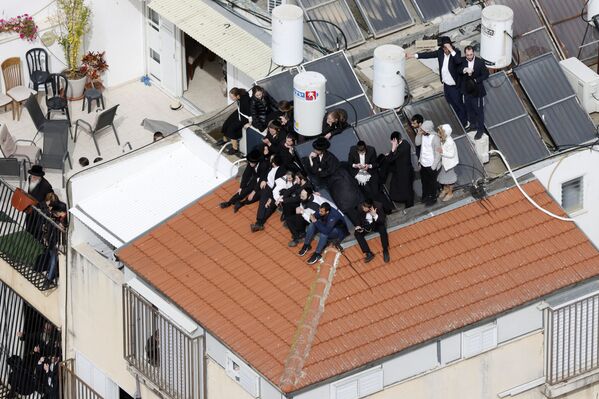 مشيعون يهود متشددون ينتظرون على سطح أحد المنازل خارج مقبرة بونيفيج في مدينة بني باراك بالقرب من تل أبيب، وسط إسرائيل، خلال جنازة الحاخام الحريديم حاييم كانيفسكي، 20 مارس 2022 - سبوتنيك عربي