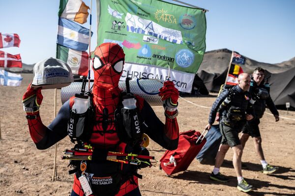 متسابق يرتدي زي شخصية سلسلة أفلام "سبايدرمان" (الرجل العنكبوت) عند وصوله مع أمتعته قبل أن يستقر في إقامة مؤقتة عشية انطلاق النسخة الـ36 من ماراثون الرمال في الصحراء المغربية في تمغالين، وسط المغرب، 26 مارس 2022. - سبوتنيك عربي
