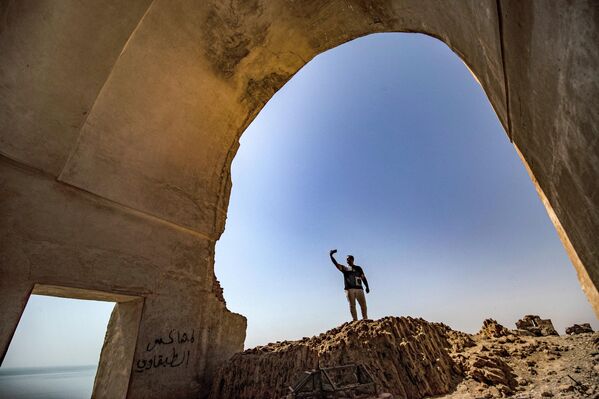 رجل يستخدم هاتفه لالتقاط صورة لأطلال قلعة جعبر في خزان بحيرة الأسد بمحافظة الرقة في 3 يونيو 2022 - سبوتنيك عربي