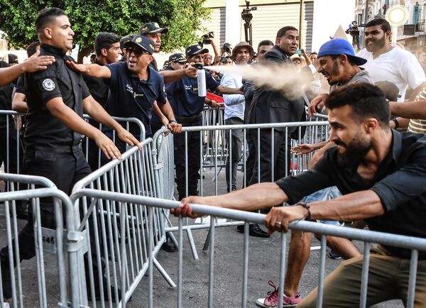 شرطي تونسي يرش الغاز المسيل للدموع على متظاهر حاول إزالة الحواجز المعدنية في 22 يوليو 2022، خلال مظاهرة على طول شارع الحبيب بورقيبة في العاصمة تونس، ضد رئيسهم والاستفتاء الدستوري المقبل في 25 يوليو. - سبوتنيك عربي