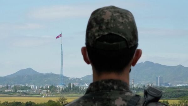علم كوريا الشمالية يرفرف في مهب الريح بينما يقف جندي من الجيش الكوري الجنوبي في حراسة قرى بانمونجوم الحدودية في باجو، كوريا الجنوبية، 4 أكتوبر 2022. - سبوتنيك عربي