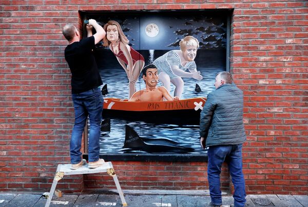 لوحة جدارية للفنان سياران غالاغر، تصور ريشي سوناك على متن زورق يدعى "آر إم إس تيتانيك"، التشبث بالحياة العزيزة في المياه التي تنتشر فيها أسماك القرش، بينما يستعد كل من بوريس جونسون وبيني موردونت للقفز في البحر، الذي تم الكشف عنه بعد فوز سوناك في انتخابات قيادة حزب المحافظين ليصبح رئيس الوزراء الجديد،  بلفاست، آيرلندا الشمالية، 28 أكتوبر 2022 - سبوتنيك عربي