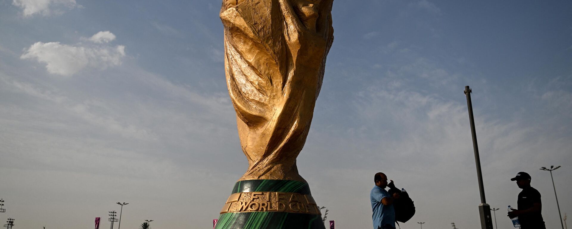 رجال يمشون أمام نسخة طبق الأصل من كأس العالم لكرة القدم خارج استاد أحمد بن علي في الريان في 12 نوفمبر 2022 ، قبل بطولة كأس العالم لكرة القدم قطر 2022. - سبوتنيك عربي, 1920, 24.11.2022