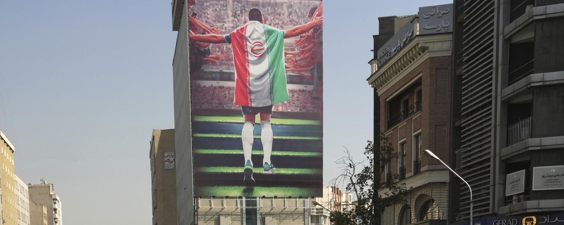 لوحة جدارية ترعاها الدولة تظهر لاعب كرة قدم وطني مع علم الدولة يدخل إلى ملعب معلقة على مبنى في وسط مدينة طهران، إيران، 22 نوفمبر 2022 - سبوتنيك عربي, 1920, 16.07.2023