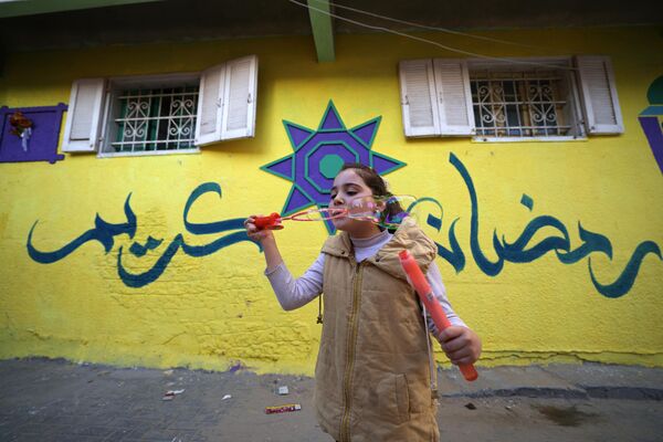 فتاة تلعب بفقاعات الصابون على خلفية منزل كتب على جدرانه رمضان كريم كجزء من مبادرة لفنان فلسطيني، في حي الزيتون بمدينة غزة، قطاع غزة، فلسطين 12 مارس  2023. - سبوتنيك عربي