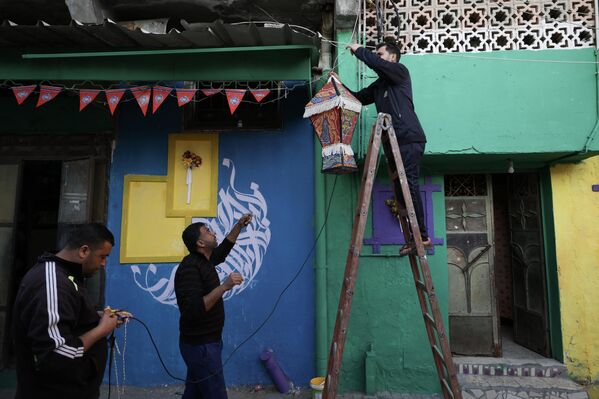 رجل يعلق فانوس رمضان على جدار مدهون بألوان زاهية كجزء من مبادرة لفنان فلسطيني، في حي الزيتون بمدينة غزة، قطاع غزة، فلسطين، 12 مارس 2023. - سبوتنيك عربي