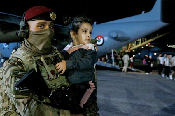 جندي يحمل طفلاً أثناء نزول أشخاص تم إجلاؤهم من السودان من طائرة في مطار عسكري في عمان في 24 أبريل 2023.  - سبوتنيك عربي