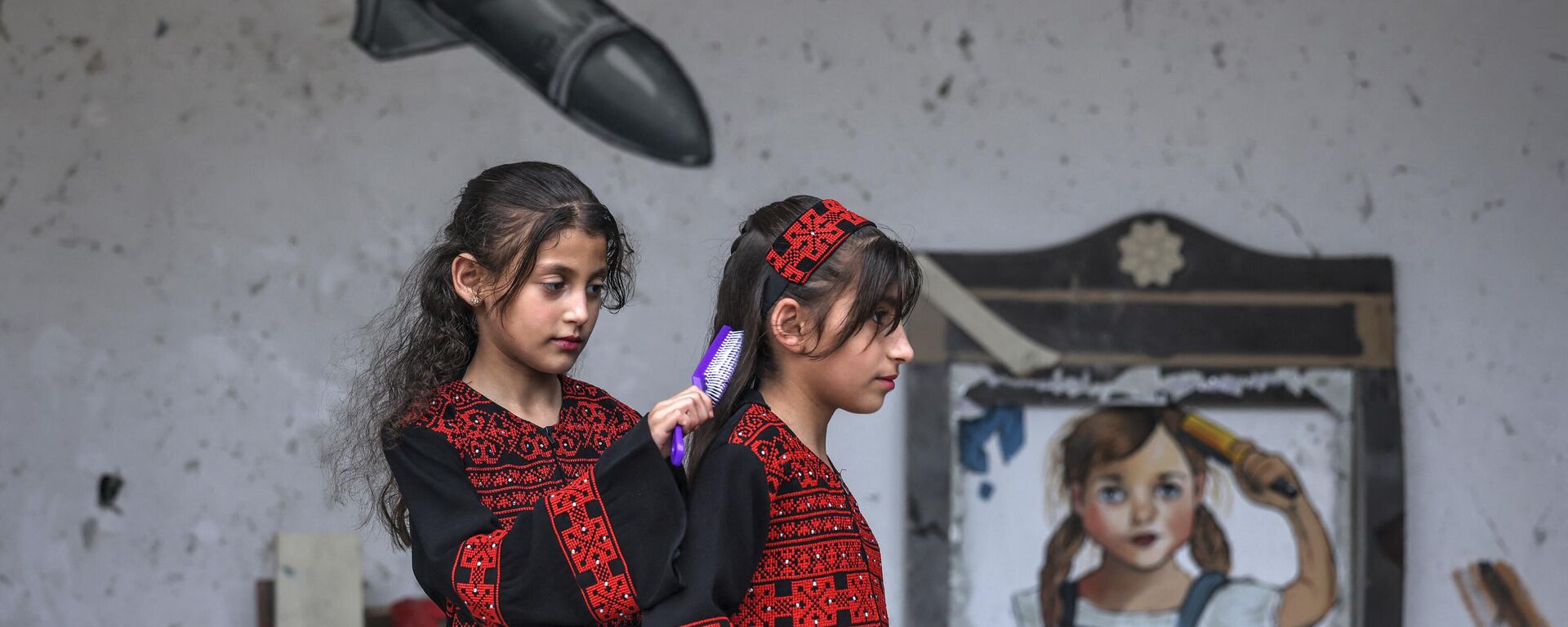 Палестинская девочка расчесывает волосы другой перед фреской во время выставки под названием Oккупация убивает детство в Газе, Палестина - سبوتنيك عربي, 1920, 09.06.2023