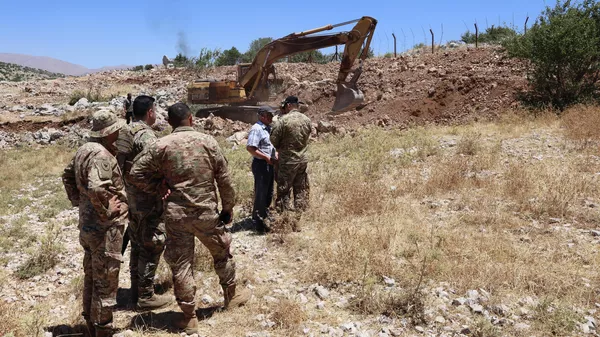 جنود من الجيش اللبناني يقفون على طول السياج الشائك الذي يحدّد الحدود بين لبنان (في المقدمة) وإسرائيل (في الخلفية) بينما تقوم حفارة من بلدية كفرشوبا بجنوب لبنان بإزالة الأرض لفتح طريق بالقرب من الخط الأزرق ، احتجاجًا على أعمال البناء الإسرائيلية المجاورة ، في 21 يوليو  2023. - سبوتنيك عربي