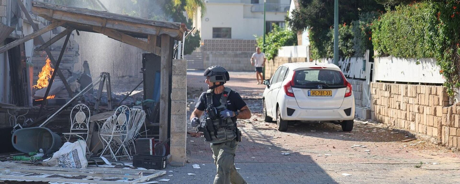 أحد أفراد القوات الإسرائيلية يمر أمام حريق مشتعل في منزل في عسقلان، في أعقاب هجوم صاروخي من قطاع غزة على جنوب إسرائيل، 7 أكتوبر/ تشرين الأول 2023 - سبوتنيك عربي, 1920, 13.10.2023
