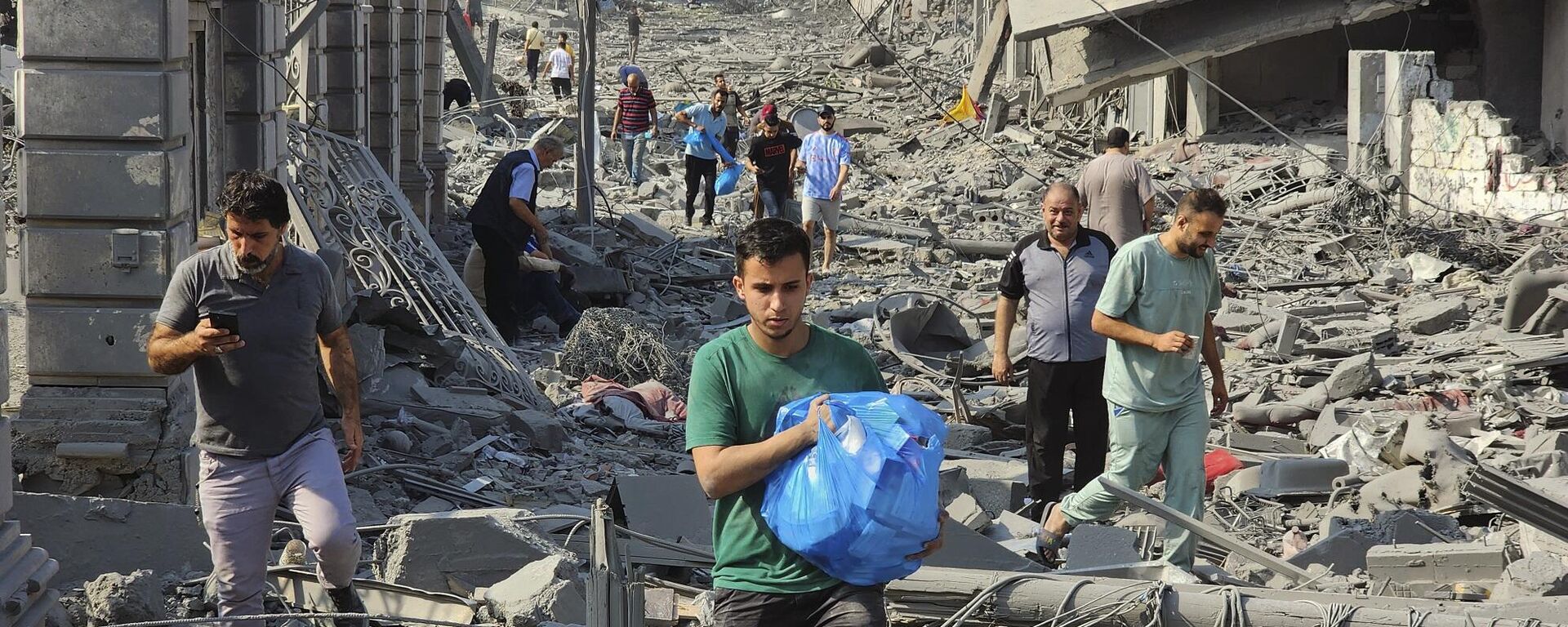 فلسطينيون يسيرون بين أنقاض المباني التي دمرتها الغارات الجوية الإسرائيلية في غزة، 10 أكتوبر/ تشرين الأول 2023 - سبوتنيك عربي, 1920, 21.10.2023