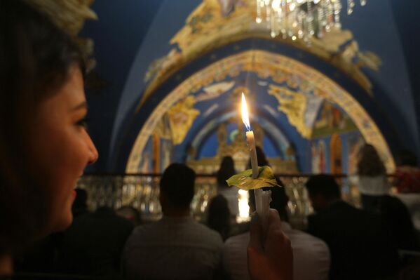 فلسطيني مسيحي أرثوذكسي يحمل شمعة مضاءة من 'النار المقدسة' في كنيسة القديس برفيريوس في مدينة غزة في أوائل 8 أبريل  2018 خلال احتفالات عيد الفصح. - سبوتنيك عربي