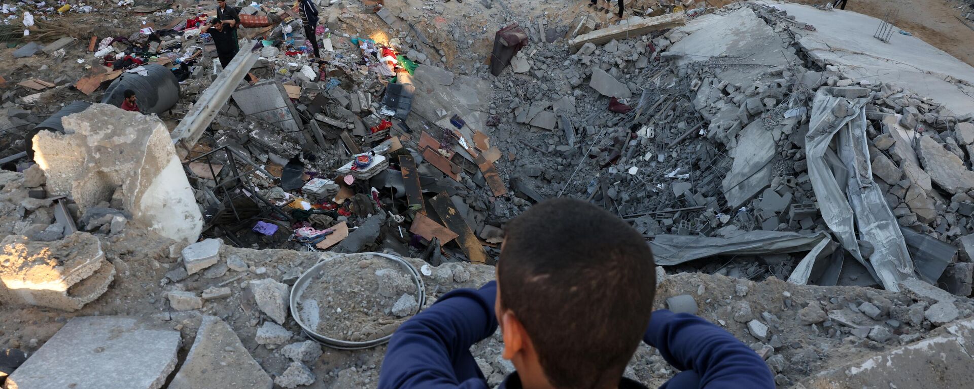 صبي صغير ينظر بينما يقوم الناس بفحص أنقاض مبنى دمر في قصف إسرائيلي في رفح جنوب قطاع غزة، 21 أكتوبر 2023. - سبوتنيك عربي, 1920, 23.10.2023
