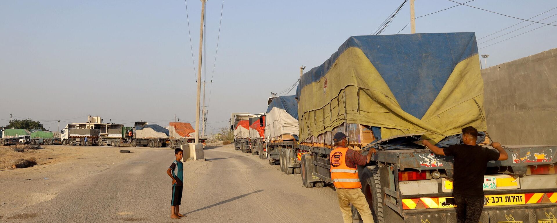 أشخاص يفرغون مساعدات إنسانية على قافلة شاحنات تدخل قطاع غزة من مصر عبر معبر رفح الحدودي في 21 أكتوبر 2023. - سبوتنيك عربي, 1920, 02.11.2023