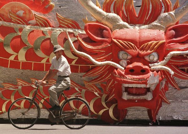 رجل صيني يمر بالدراجة بجوار مجسم عليه رأس تنين تم استخدامه خلال أحد العروض للاحتفال باستعادة هونغ كونغ، المشهد خارج استاد العمال في بكين يوم الجمعة 4 يوليو 1997. - سبوتنيك عربي