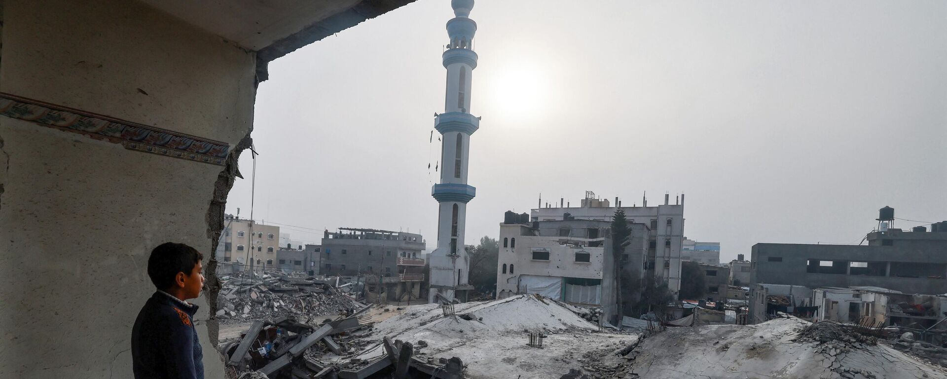طفل يقف داخل مبنى متضرر ويحدق  بمسجد الفاروق، الذي دمره القصف الإسرائيلي في رفح بجنوب قطاع غزة. - سبوتنيك عربي, 1920, 13.05.2024