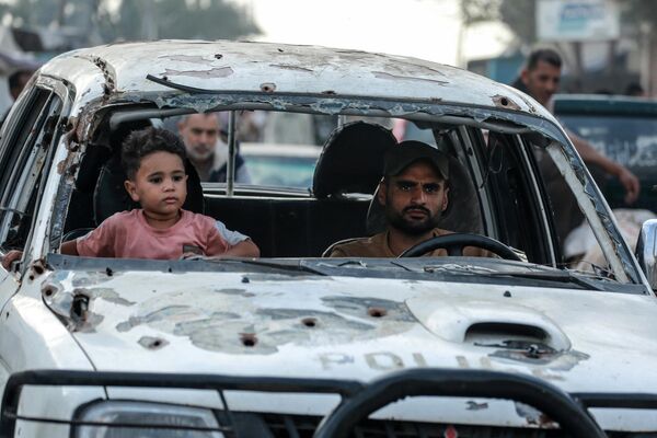 طفل فلسطيني يجلس بجوار رجل يقود سيارة متضررة في دير البلح وسط قطاع غزة في 1 مايو 2024. - سبوتنيك عربي