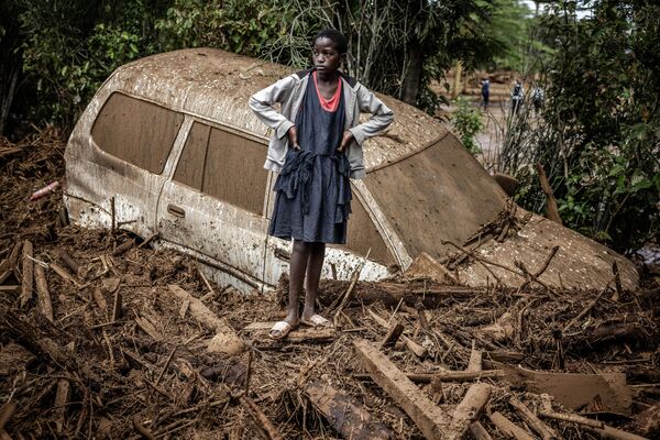 فتاة تقف بجوار سيارة مدفونة في الوحل في منطقة تأثرت بشدة بالأمطار الغزيرة والفيضانات المفاجئة في قرية كاموتشيري البكينية في 29 أبريل 2024 - سبوتنيك عربي