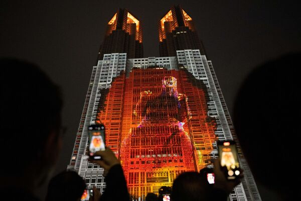 يلتقط الناس صورًا لمبنى حكومة مدينة طوكيو، مضاءً بخريطة عرض بعنوان &quot;غودزيلا: الهجوم على طوكيو&quot; والتي تُظهر عرضًا بالحجم الطبيعي بطول 100 متر لغودزيلا في طوكيو في 27 أبريل 2024. - سبوتنيك عربي