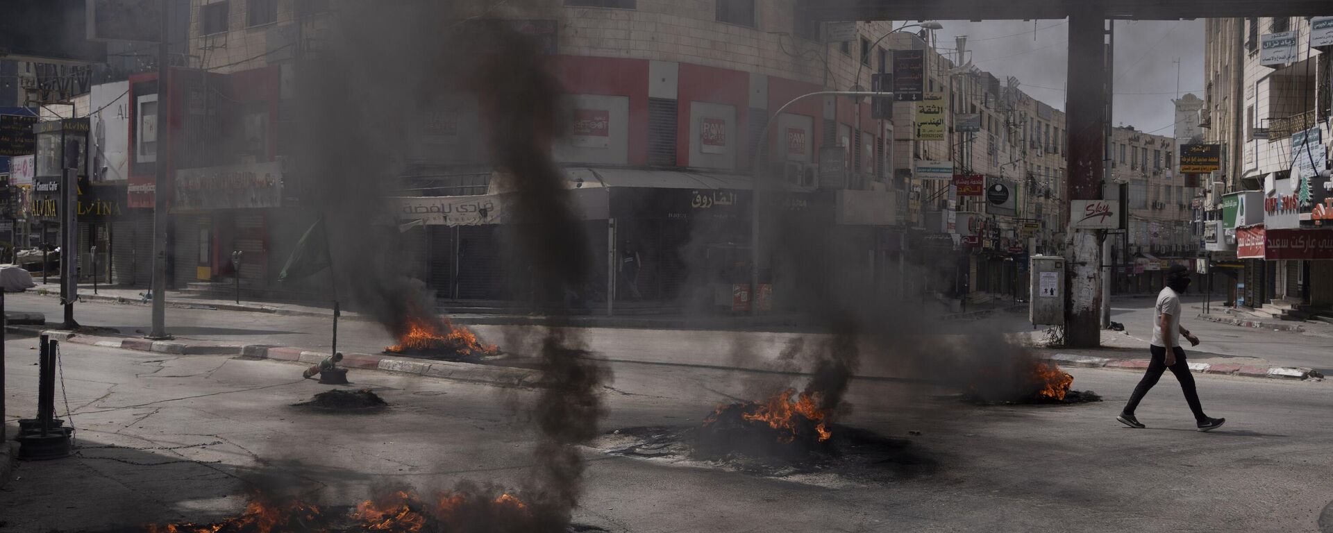رجل فلسطيني يسير بجوار إطارات مشتعلة خلال اشتباكات مع القوات الإسرائيلية في مدينة جنين بالضفة الغربية، 22 مايو 2024 - سبوتنيك عربي, 1920, 27.06.2024