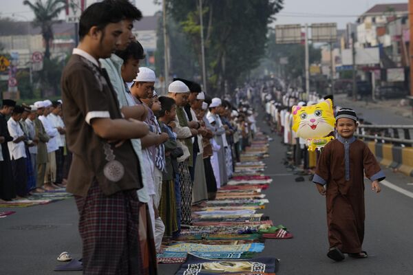 صبي يحمل بالونًا، بينما يؤدي المصلون صلاة عيد الأضحى في أحد شوارع جاكرتا، إندونيسيا، 17 يونيو 2024 - سبوتنيك عربي