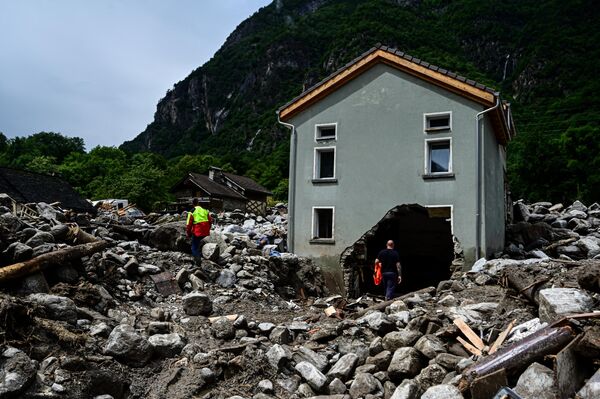 عمال يقفون بين الأنقاض والحجارة خارج منزل في قرية سورت، سويسرا، نتيجة الأمطار الغزيرة. - سبوتنيك عربي
