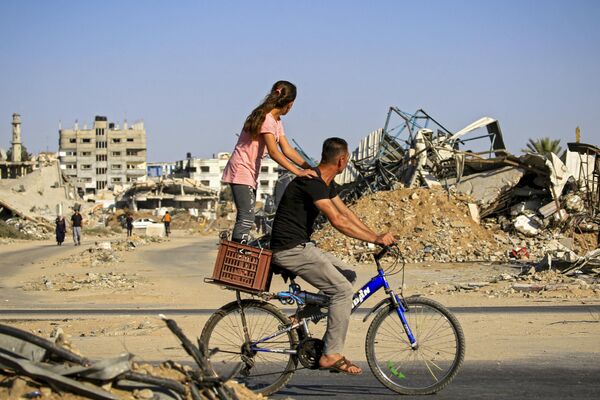 فتاة تركب دراجة هوائية أمام أنقاض المباني التي دمرت خلال القصف الإسرائيلي على مخيم البريج للاجئين وسط قطاع غزة. - سبوتنيك عربي