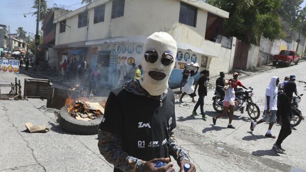 متظاهر ملثم يسير أمام حاجز طريق مشتعل وضعه المتظاهرون للمطالبة بأن تتخذ الشرطة ورئيس الوزراء إجراءات فورية ضد العصابات في بورت أو برنس في هايتي. - سبوتنيك عربي