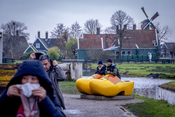 سائحون آسيويون يجلسون في أحذية هولندية خشبية كبيرة الحجم، في متحف طواحين الهواء في زانسي شان، هولندا. - سبوتنيك عربي