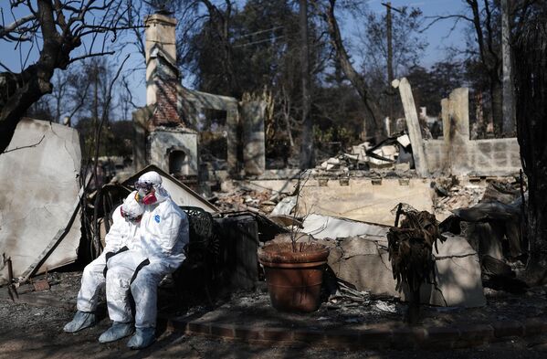 زوجان يرتديان ملابس واقية كاملة أثناء البحث في بقايا منزلهما الذي احترق في حريق إيتون في ألتادينا، كاليفورنيا. - سبوتنيك عربي