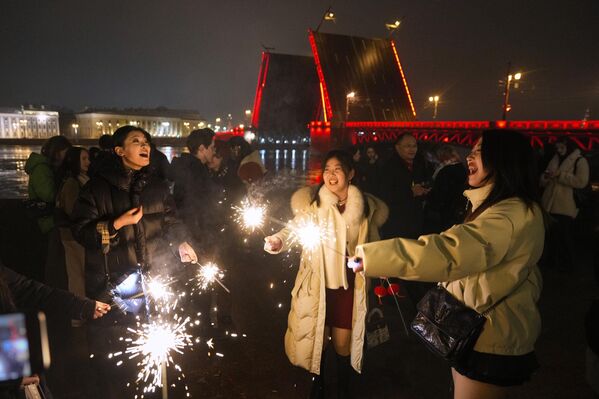 المحتفلون يشعلون الألعاب النارية بالقرب من جسر القصر على نهر نيفا، والذي تم رفعه وإضاءته خلال احتفالات رأس السنة القمرية الجديدة في سانت بطرسبرغ، روسيا - سبوتنيك عربي