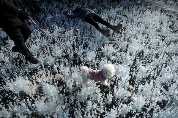 رجل يمشي مع كلبه بينما يرقد طفل على بحيرة متجمدة في منطقة جبلية ذات مناظر خلابة خلال عطلة رأس السنة الصينية في مييون، شمال بكين.  - سبوتنيك عربي